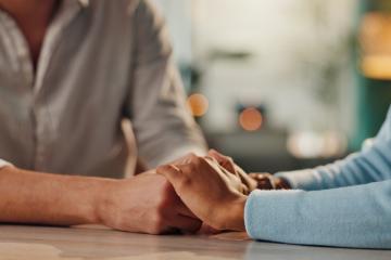 Two people holding hands for comfort across a table