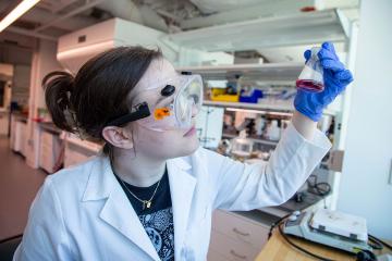 A Simmons student wearing goggles and working in the chemistry lab