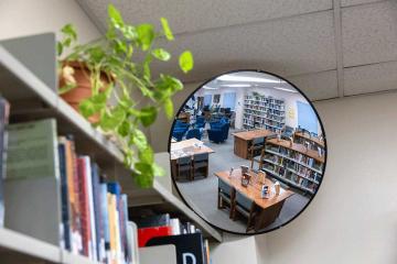 A bookshelf containing books and a plant as well as a round mirror that is reflecting a room in the library. Photo courtesy of the Colorado State Library – Colorado Department of Education