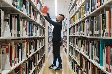 Student grabbing book in the library shelves.