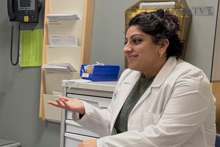 A Simmons Nursing alum wearing a white coat and gesturing as she speaks with a patient 