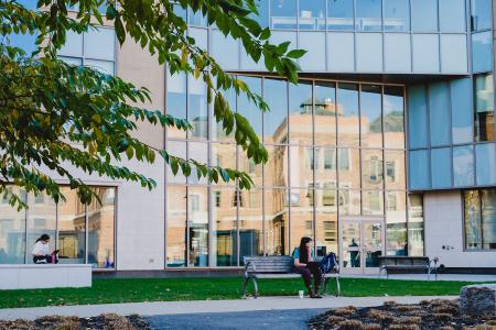 A student sits on a bench outside a building on the Simmons University campus