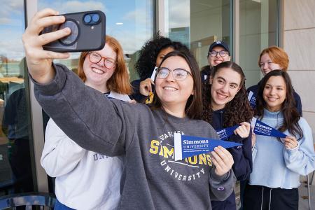 A group of Simmons undergraduates taking a selfie and holding Simmons banners