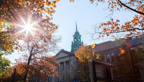 The cupola of the Main College Building on the Simmons University campus, as seen through a tree with colorful fall leaves.