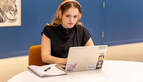 A Simmons graduate student wearing headphones while working on a laptop