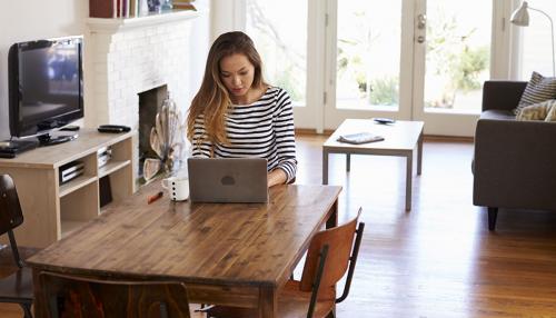 A woman working on a laptop while seated at a dining table