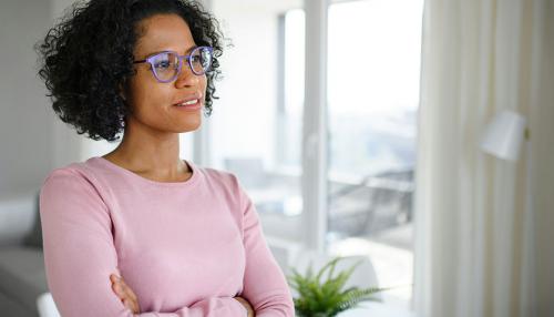 A woman wearing a pink sweater, arms crossed, looking off to the right.