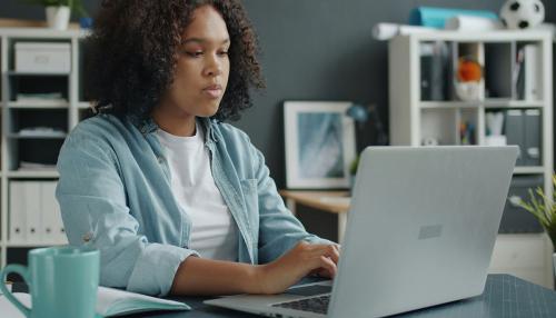 A young woman wearing a teal shirt sitting at a table working on a laptop