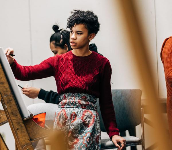 Student standing by easel painting in classroom