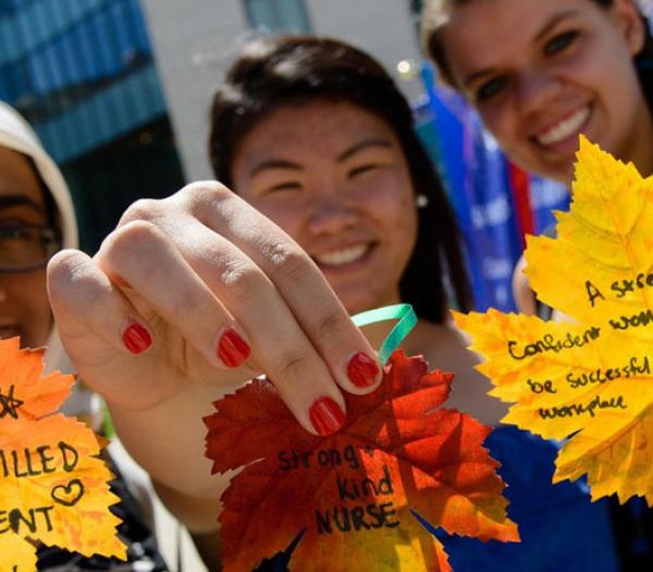 A group of three students holding up colorful fall leaves with their aspirations written on them