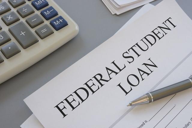 A paper on a desk that is labeled Federal Student Loan. A calculator sit nearby.