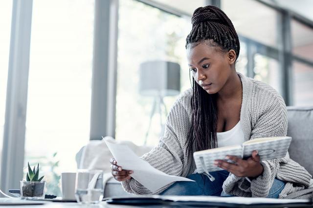 A young woman with paperwork in one hand and a notebook in the other