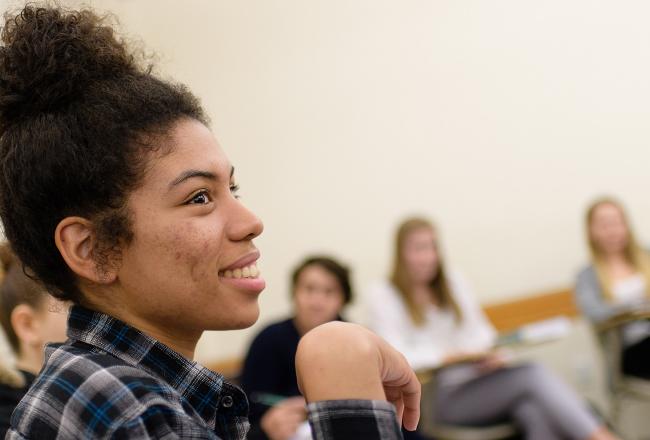 A student sitting in class with additional students sitting behind her.