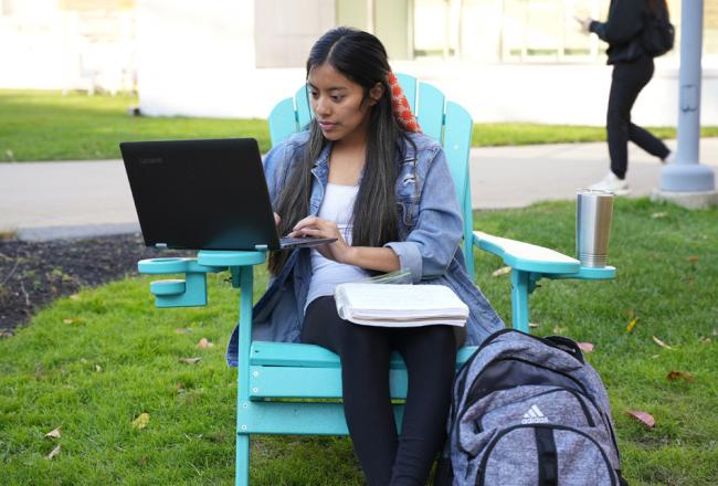 student sitting outside on sunny day with laptop and backback
