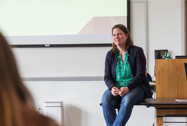 Simmons faculty member Noelle Dimitri seated on a table while engaging with a class in the Simmons School of Social Work