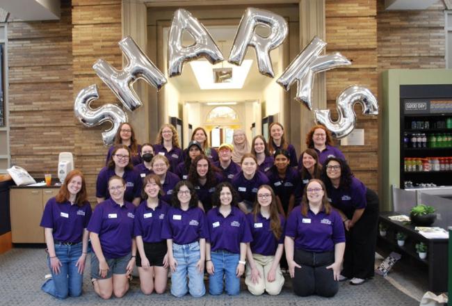 A group of 2025 orientation leaders posing in front of balloons that spell out SHARKS