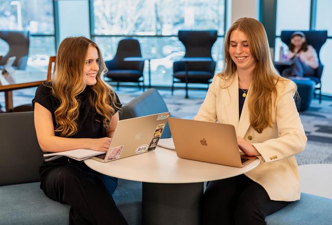 Two Simmons graduate students seated at a table with their laptops open