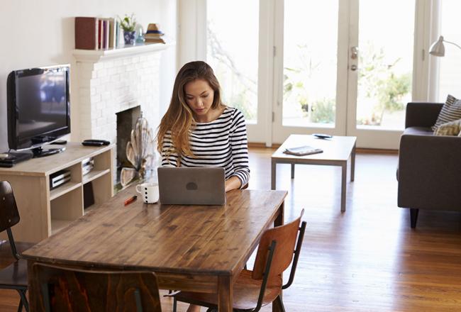 A woman working on a laptop while seated at a dining table