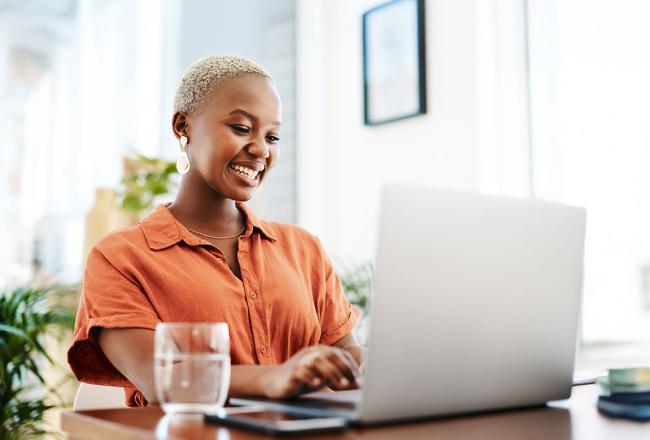 A woman wearing an orange shirt while seated at a desk working on a laptop