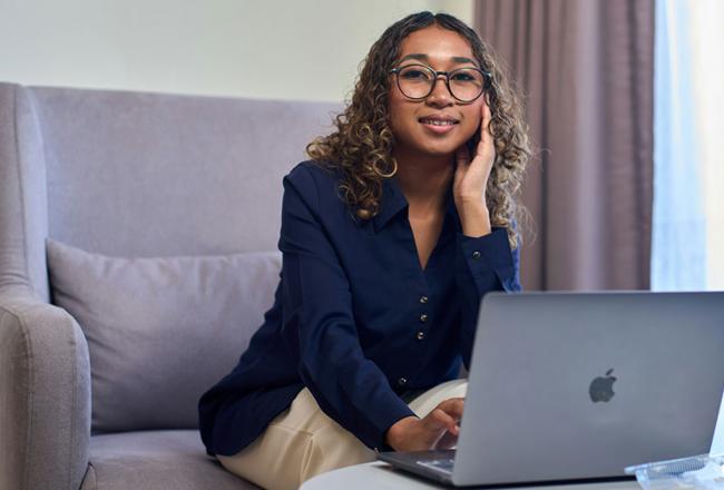 A young woman wearing a blue blouse working on a laptop at a table