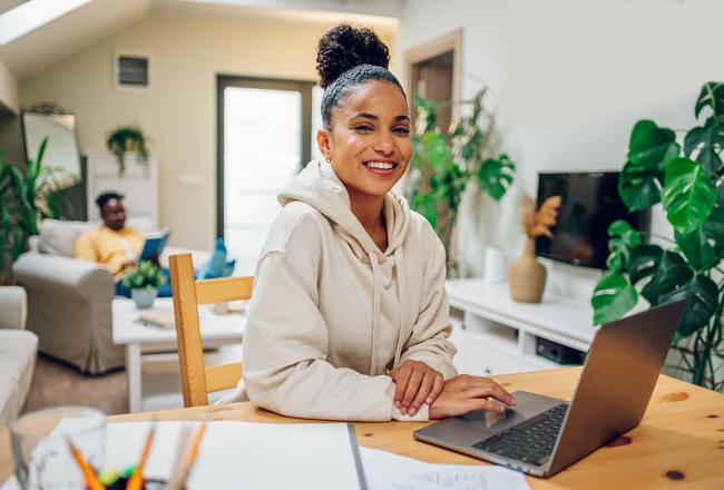 A young woman working ona laptop in her living room surrounded by plants