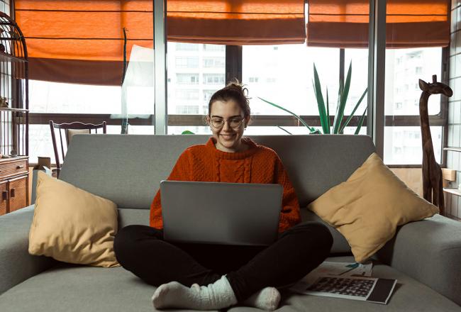 A young woman seated cross-legged on a couch while using a laptop. Courtesy of unsplash.