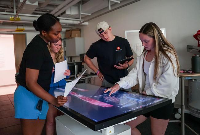 Four Simmons physical therapy students working at an anatomage table