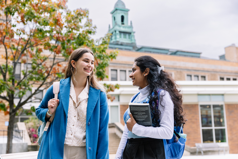 Two Simmons students walking on campus with a view of the iconic cupola in the background