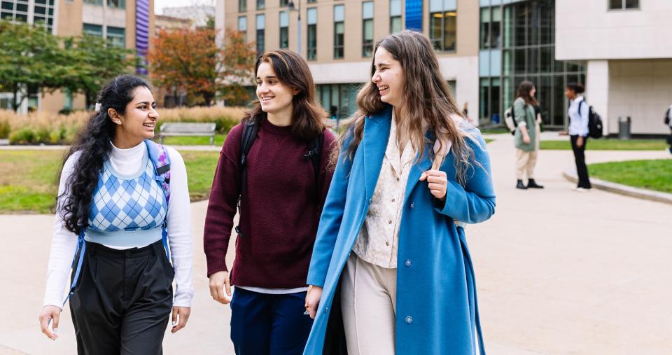 Three smiling Simmons students walking together through the Main Campus Quad