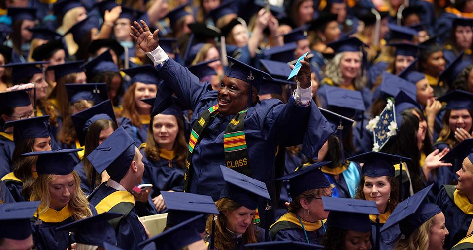 Graduate Student standing cheering amongst fellow graduates