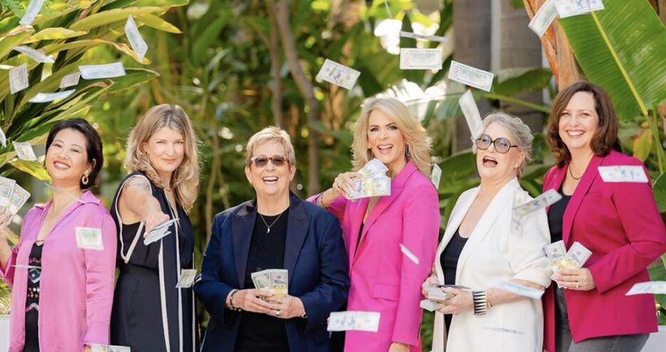 Six women dressed professionally and holding stacks of money