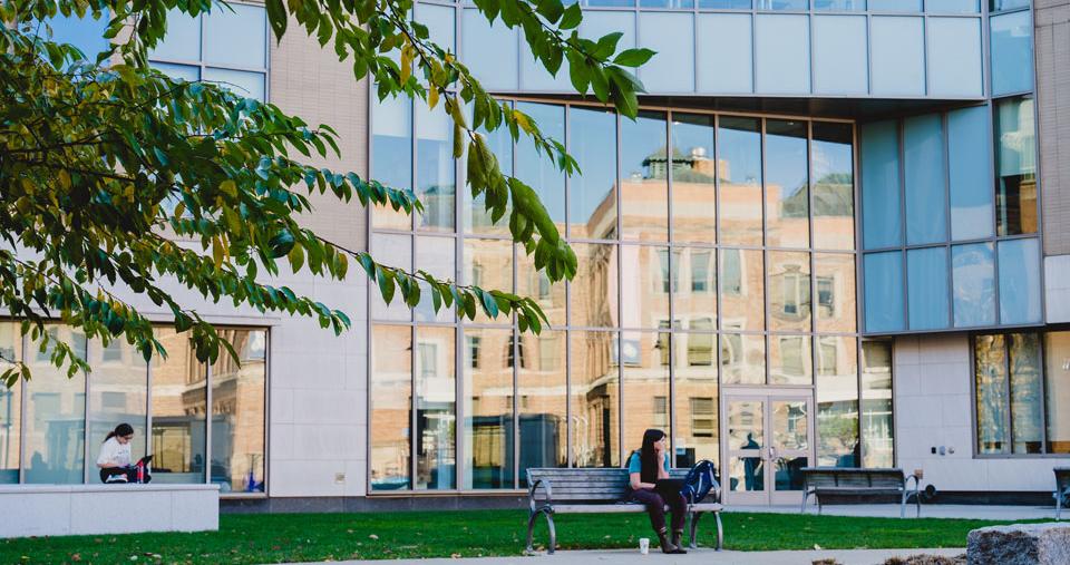 A student sits on a bench outside a building on the Simmons University campus