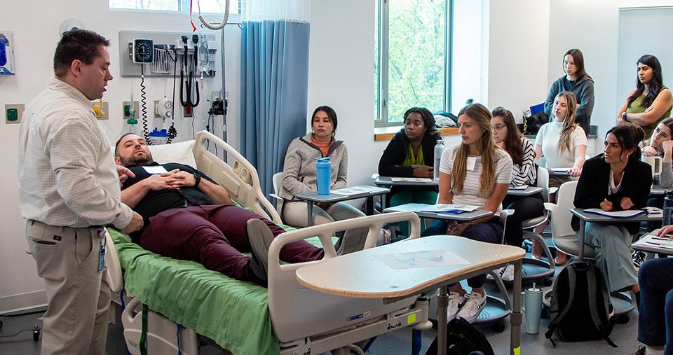 Nursing Students in classroom featuring practice patient in hospital bed