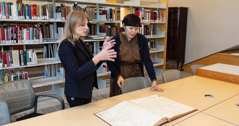 Two SLIS students standing at a table discussing an archival document