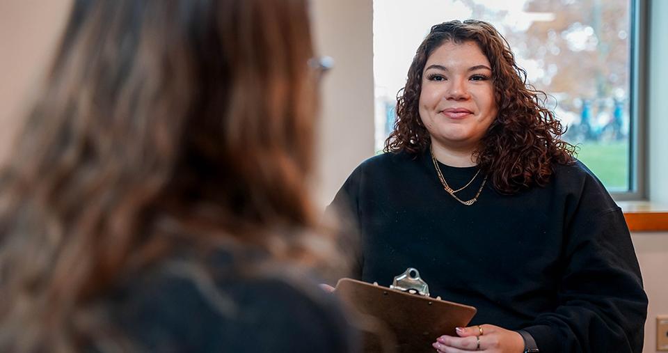 Person holding clipboard speaking to another person