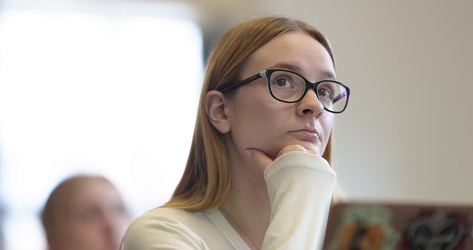 Student with glasses sitting and listening in classroom.