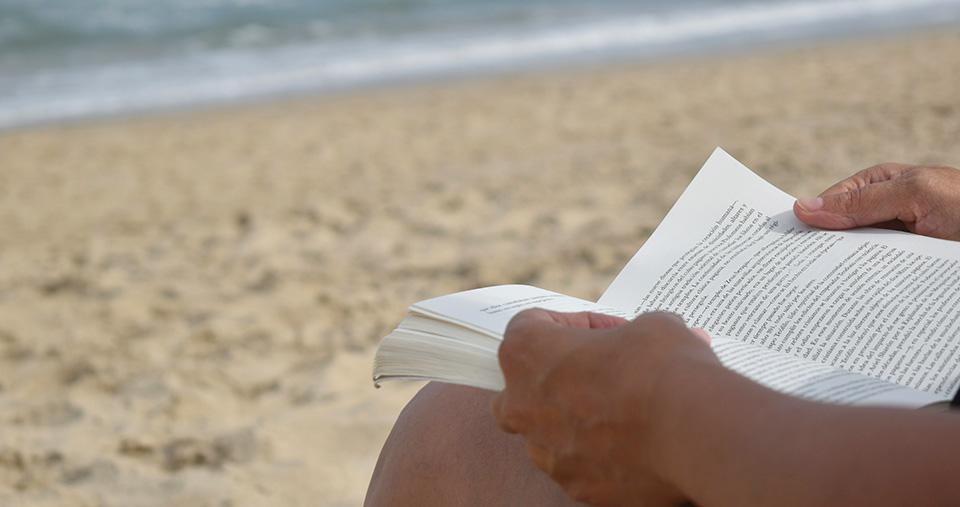Hands of person holding book on beach. Photo by Pedro Fleitas.