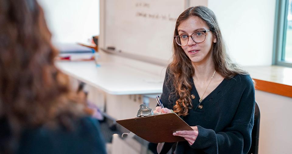 A student holding a clipboard talking to another student