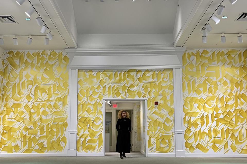 Sneha Shrestha standing in front of the site specific (temporary) artwork she created directly on the walls of the Trustman Gallery in 2019 for her show Golden Equinox.