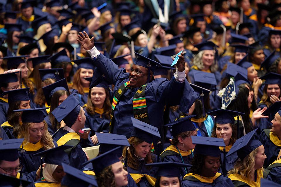 Graduate Student standing cheering amongst fellow graduates
